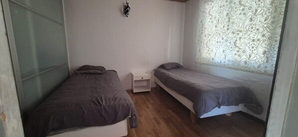 A small room with two single beds, a nightstand, and a window with patterned curtains.