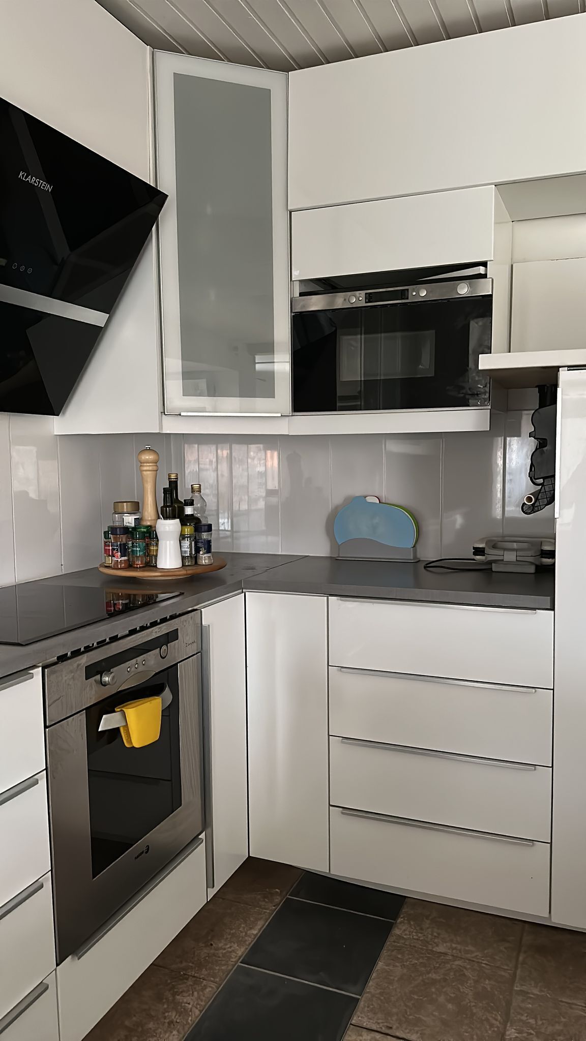 Une cuisine moderne avec des meubles blancs, un four encastré et un four à micro-ondes.