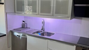 Cozinha moderna com pia de aço inoxidável, armários brancos e lava-louças.