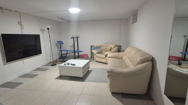 Uma sala de estar com televisão de tela plana, sofá, mesa de centro e uma poltrona.