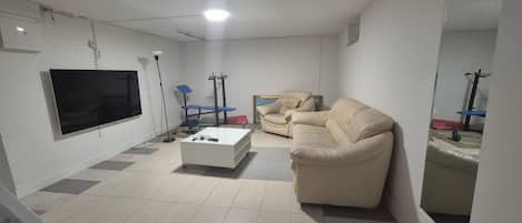 A living room with a flat-screen TV, a sofa, a coffee table, and a chair.