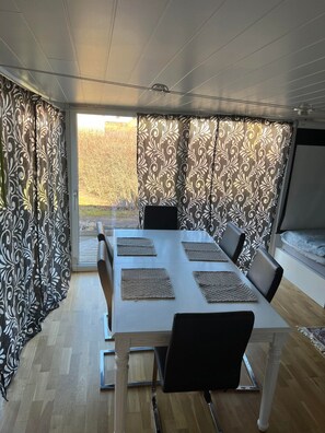 En matplats med ett vitt bord, svarta stolar och en mönstrad gardin.