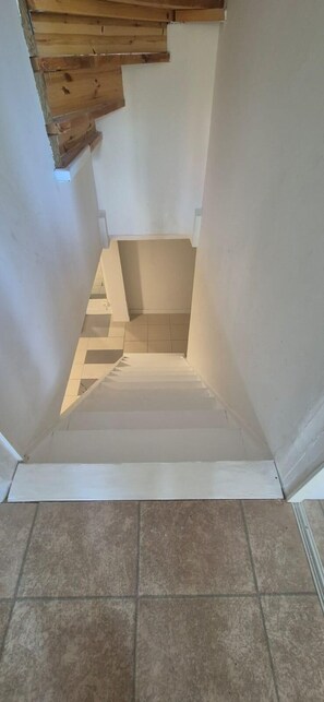 Eine Treppe mit weißer Handlauf und beigen Stufen, die zu einer Zwischenebene mit einem Holzbalken darüber führt.