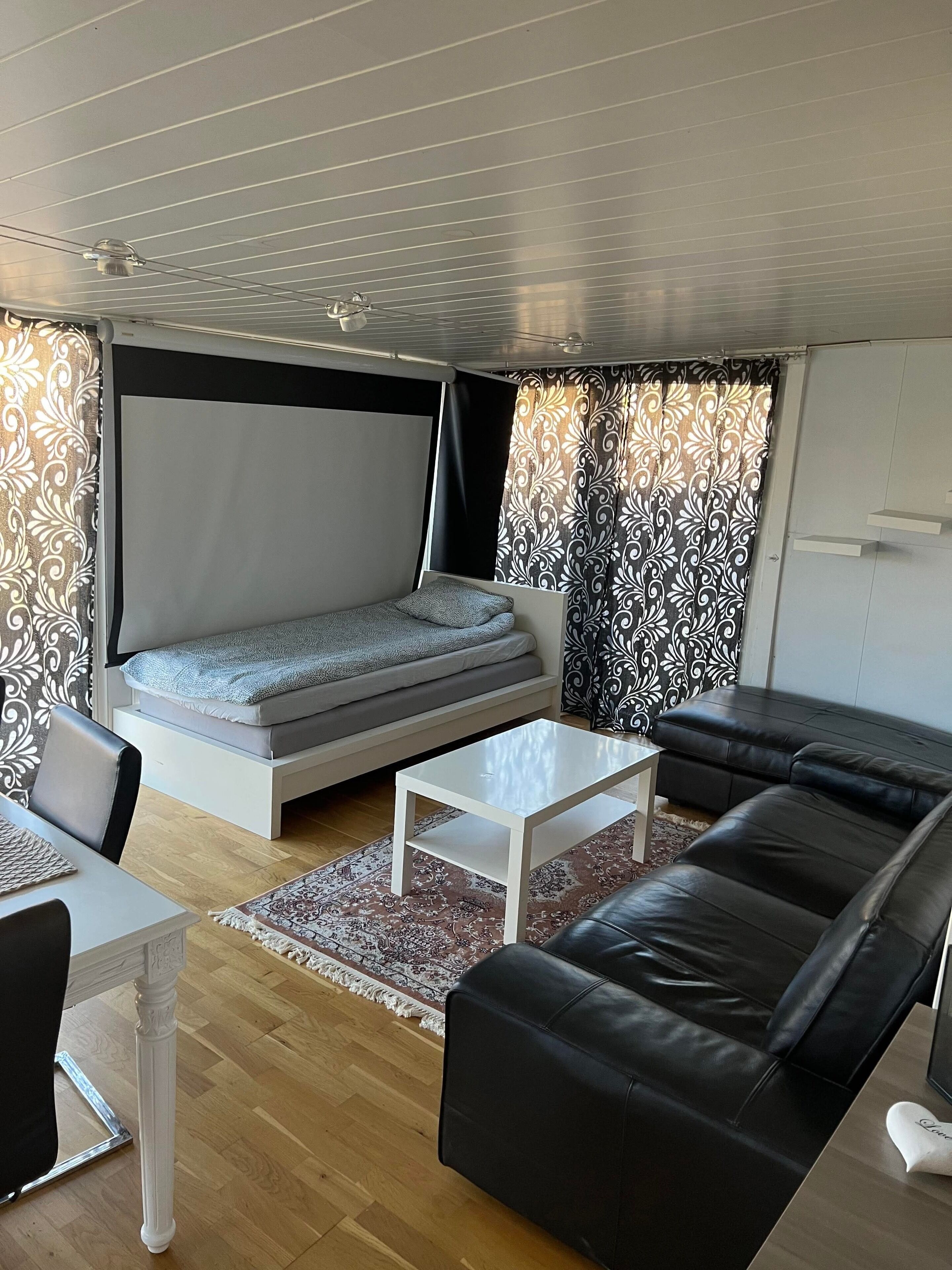 Un salon moderne avec un canapé, une table basse, un lit et des rideaux à motifs.