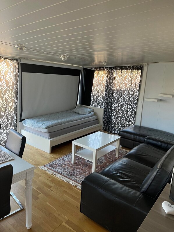 A modern living room with a sofa, a coffee table, a bed, and patterned curtains.