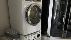 Uma área de lavanderia compacta com máquinas de lavar empilhadas e um chuveiro com divisória de vidro.