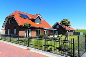 A two-story house with a red-tiled roof, a black metal fence, and a well-maintained lawn. - Holiday home in Burhave with swimming pool (Burhave)