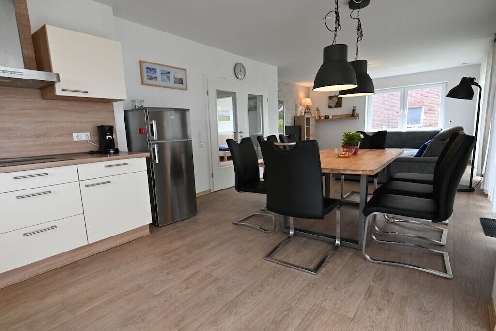 A modern kitchen with white cabinetry, a stainless steel refrigerator, and a dining area with black chairs and a wooden table.