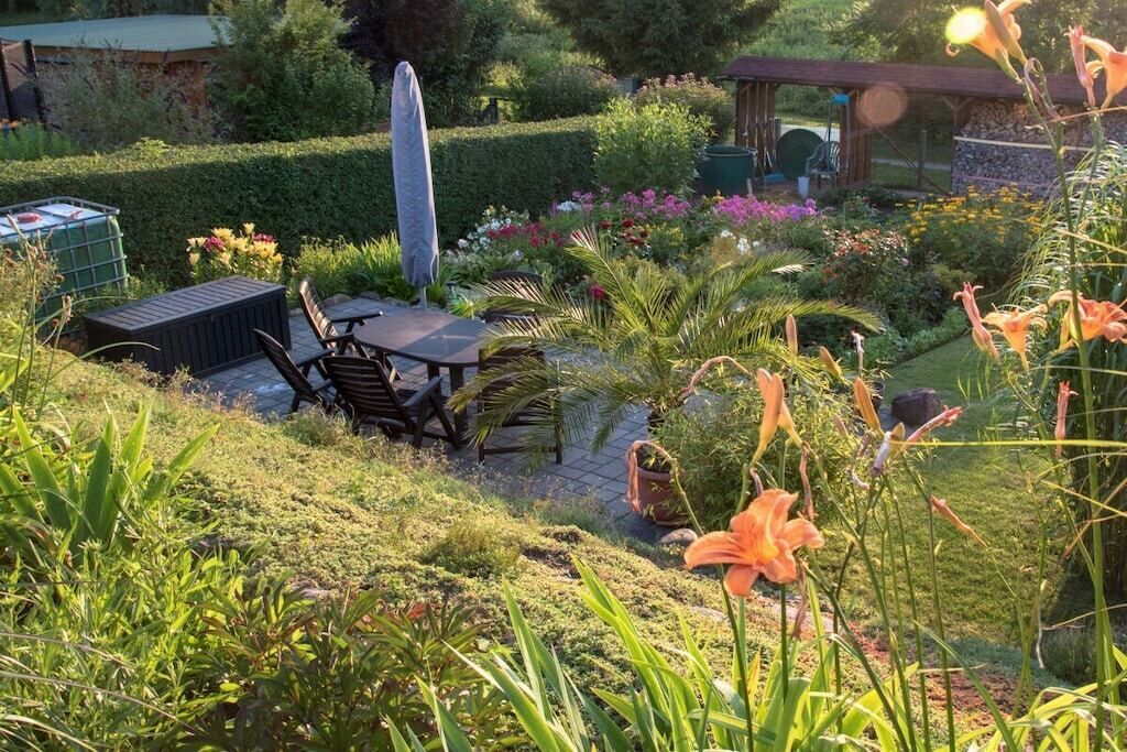 A garden with a patio table and chairs, surrounded by various plants and flowers.