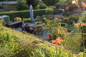 Een tuin met een patio tafel en stoelen, omgeven door diverse planten en bloemen.