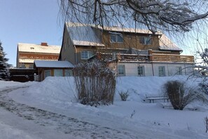 Een gebouw met twee verdiepingen en een schuin dak, omgeven door een met sneeuw bedekte grond en schaarse begroeiing.