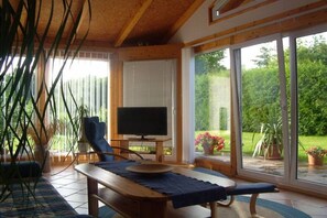A room with a television, a bench, and a table. There are large windows and a view of greenery outside. - Holidays at Bärbel Güldner's (Feldberger Seenlandschaft)