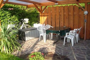 Een terras buiten met een stenen vloer, een barbecue, een tafel met stoelen en een houten omheining.