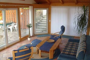 A room with a wooden bench, a sofa, and a table with a blue cushion. There is a sliding glass door leading to an outdoor area with a wooden fence and a chair. - Holidays at Bärbel Güldner's (Feldberger Seenlandschaft)
