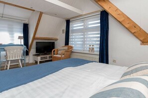 Un dormitori amb un llit, una cadira, una televisió i una finestra amb cortines.