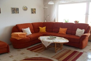 Een woonkamer met een hoekbank, een klein rond tafeltje en een vloerkleed met dessin.