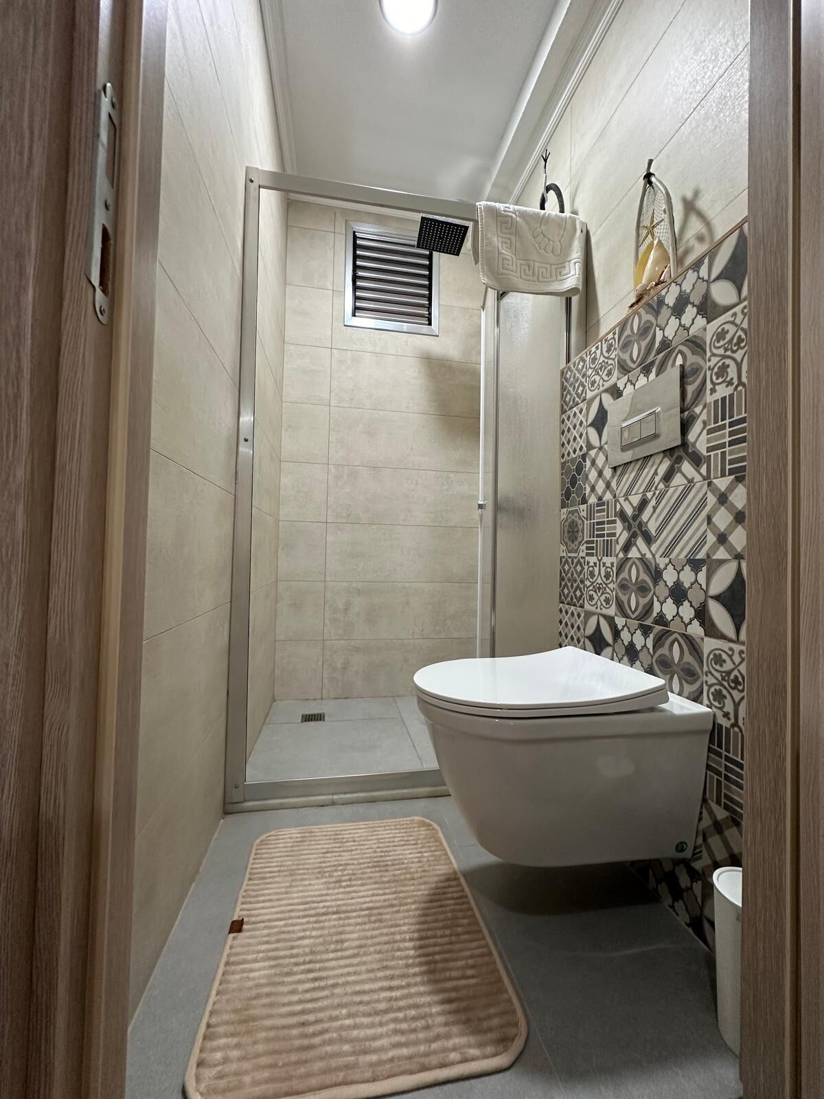 A compact bathroom with a shower, toilet, and a patterned wall.