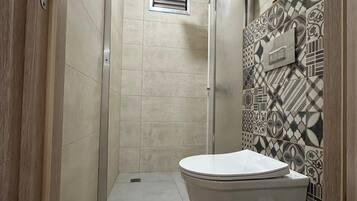 A compact bathroom with a shower, toilet, and a patterned wall.