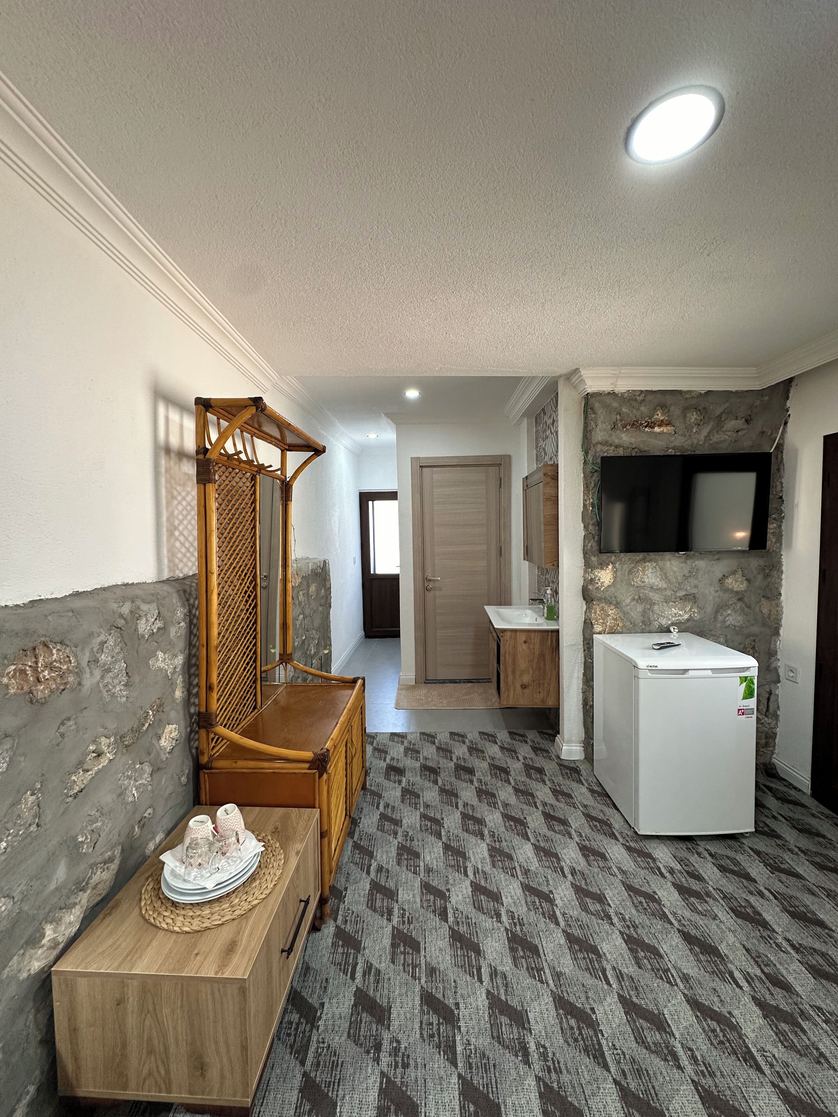 A room with a wooden bench, a small table with glasses, a white refrigerator, and a patterned carpet.