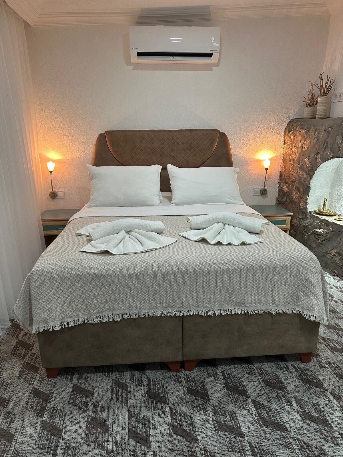 A neatly made bed with a patterned bedspread and pillows, a wall-mounted air conditioner, and two bedside lamps.