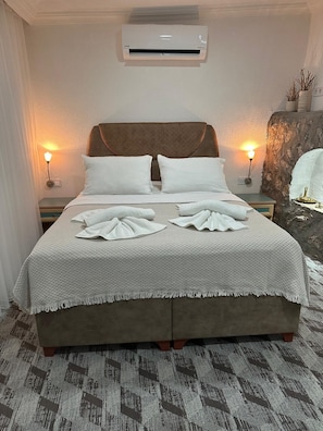 A neatly made bed with a patterned bedspread and pillows, a wall-mounted air conditioner, and two bedside lamps. - Beach Room Suite İcmeler (Marmaris)