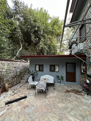 A stone-floored patio with two patterned chairs and a table, a small building with a door and windows, and a stone wall. - Beach Room Suite İcmeler (Marmaris)
