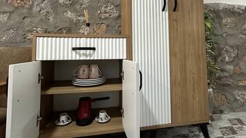 A cabinet with a wooden finish and a white interior, featuring a shelf with a red kettle and cups.