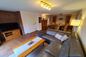 Ein Wohnzimmer mit Flachbildfernseher, einer Couch, einem Couchtisch aus Holz und einem Kamin aus Backsteinen.