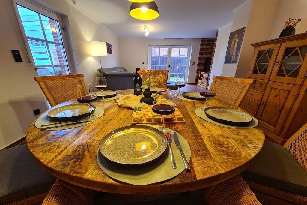 Un coin repas avec une table ronde en bois, dressée pour quatre personnes, entourée de chaises en osier.