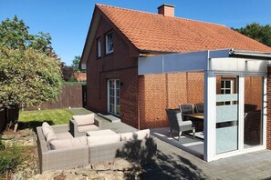 Ein Ziegelhaus mit einem Ziegeldach, einer überdachten Terrasse mit Gartenmöbeln und einem eingezäunten Garten.