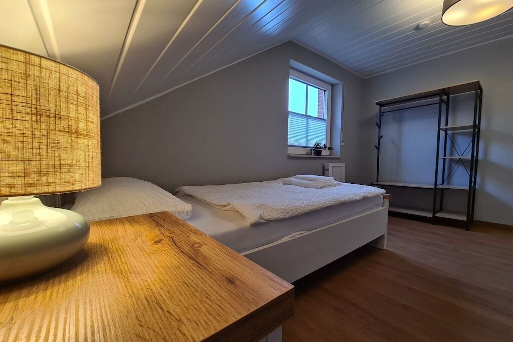 A bedroom with a bed, a bedside table with a lamp, a window with blinds, and a wardrobe.