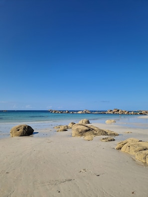 Une plage avec de gros rochers et une eau d’un bleu limpide.