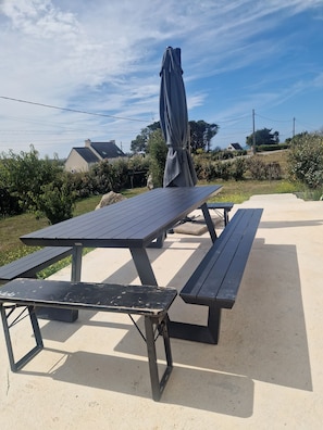 Un espace de pique-nique en plein air, avec une table et des bancs, entouré de verdure et sous un ciel dégagé.