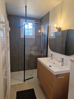 Une salle de bain moderne avec une douche à parois de verre, un lavabo blanc et un meuble-lavabo en bois.