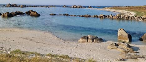 Eine Küstenlandschaft mit blauem Himmel, steinernen Felsformationen und einem Sandstrand.