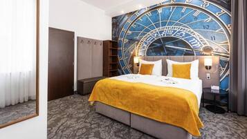 Ein Hotelzimmer mit einer großen Wanduhr, einem Bett mit gelber Decke, einem Kleiderschrank und einem Nachttisch mit einer Lampe.