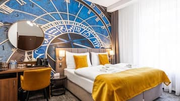 Une chambre d’hôtel avec une grande horloge murale, un lit avec une literie blanche et un plaid jaune, un bureau avec une chaise et un miroir.