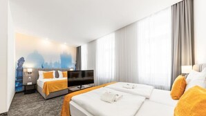 Ett hotellrum med en säng, en tv, ett nattduksbord och en vägg prydd med en väggmålning som föreställer en stadsbild.