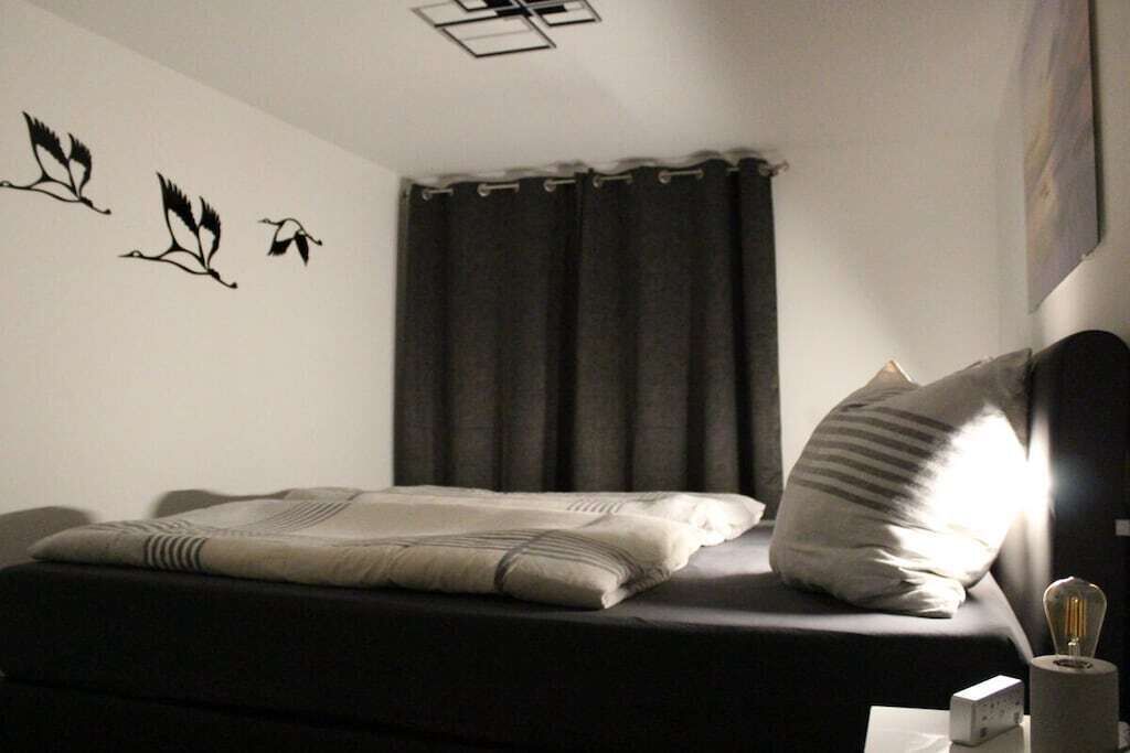 A bedroom with a bed, a wall-mounted light, a curtain, and a wall decoration.