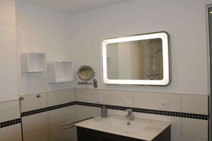Een badkamer met een witte wastafel, een spiegel met verlichting en een handdoekhouder.