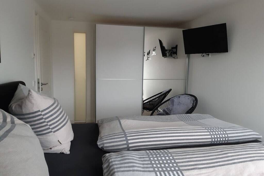 A bedroom with two beds, a wardrobe, a chair, and a flat-screen TV.