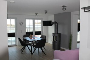Een moderne woonkamer met een eethoek, een open haard en een aan de muur bevestigde televisie.