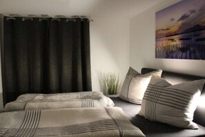 Een slaapkamer met een bed, donkere gordijnen, een aan de muur hangend schilderij en een potplant.