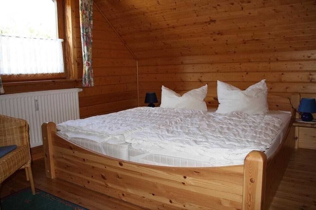 Ein Zimmer mit Holzwänden, einem Einzelbett, einem Nachttisch, einer Lampe und einem Fenster mit Vorhängen.