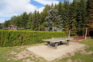 A ping pong table in a park with a swing set and a small wooden structure in the background. - Hasselfelde House 32 (Hasselfelde)