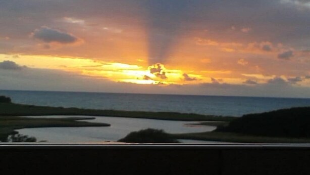 Um pôr do sol sobre a água, com uma estrada em primeiro plano.