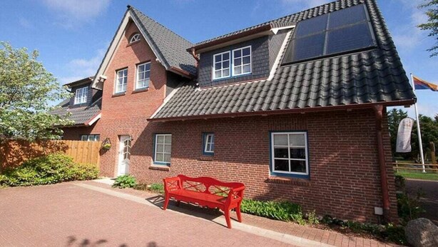A two-story brick house with a sloped roof, a red bench in the driveway, and a flag on a flagpole. - Holiday apartment in Nebel with swimming pool (Nebel)