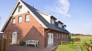 A two-story brick house with a sloped roof, a white door, and a small porch with a bench. - Holiday apartment in Nebel with swimming pool (Nebel)