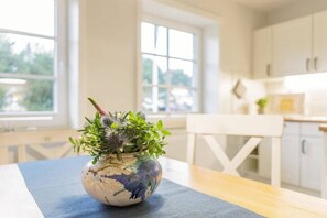 Et køkken med hvide skabe, et spisebord med en blå dug og en potteplante på bordet.