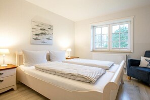 Ein Schlafzimmer mit zwei Betten, einem Fenster, einer Heizung und einem Sessel.